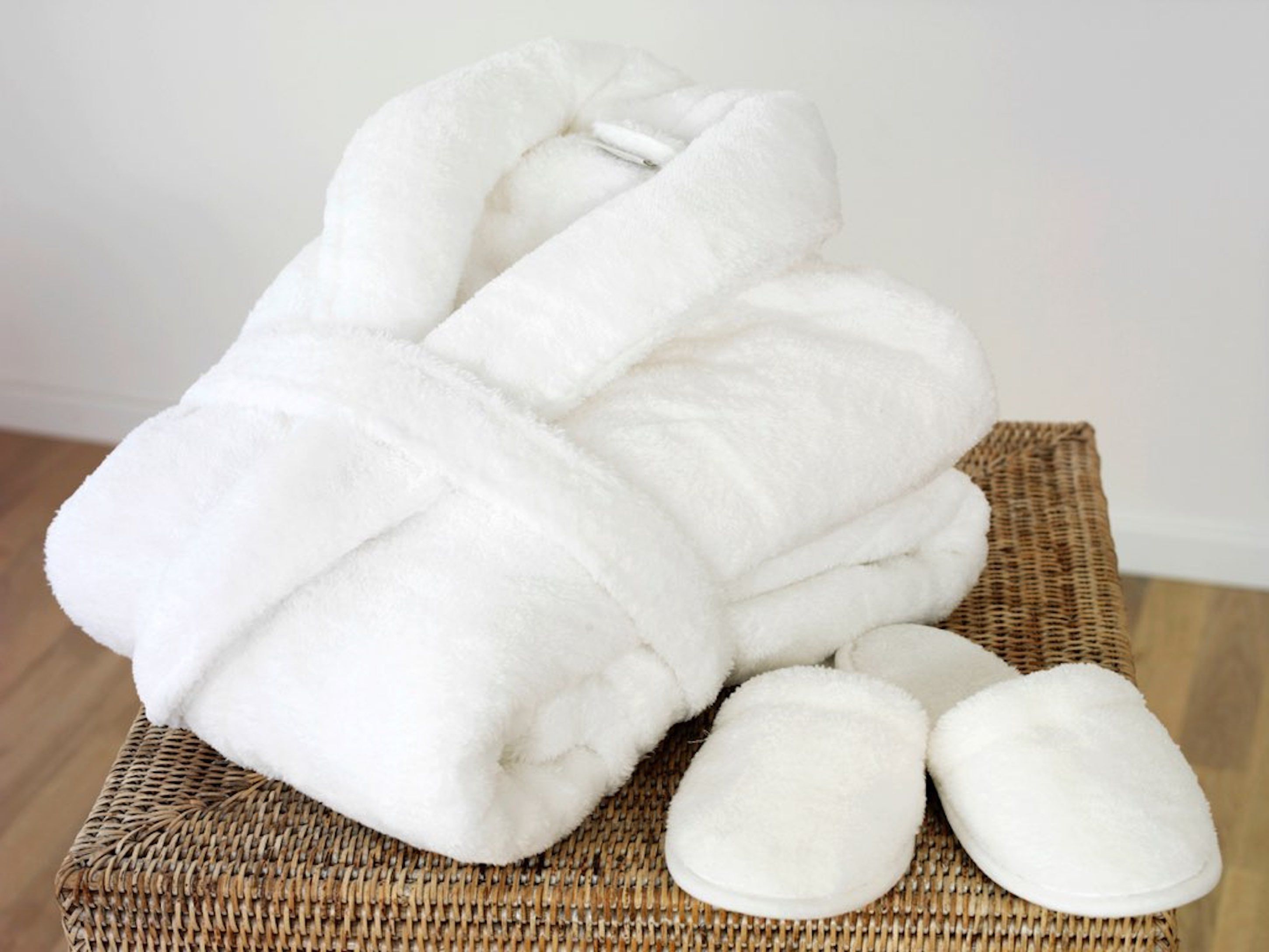 Un peignoir blanc et des chaussons sur une chaise en osier.