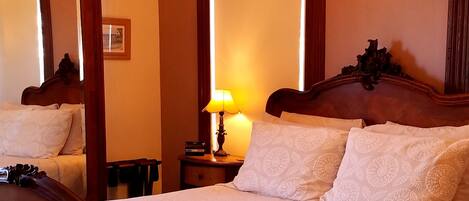 A hotel room with a large bed, a wooden headboard, a chandelier, a bedside table with a lamp, and a large mirror.