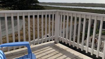 A deck with a white railing, blue chairs, and a view of a natural landscape.