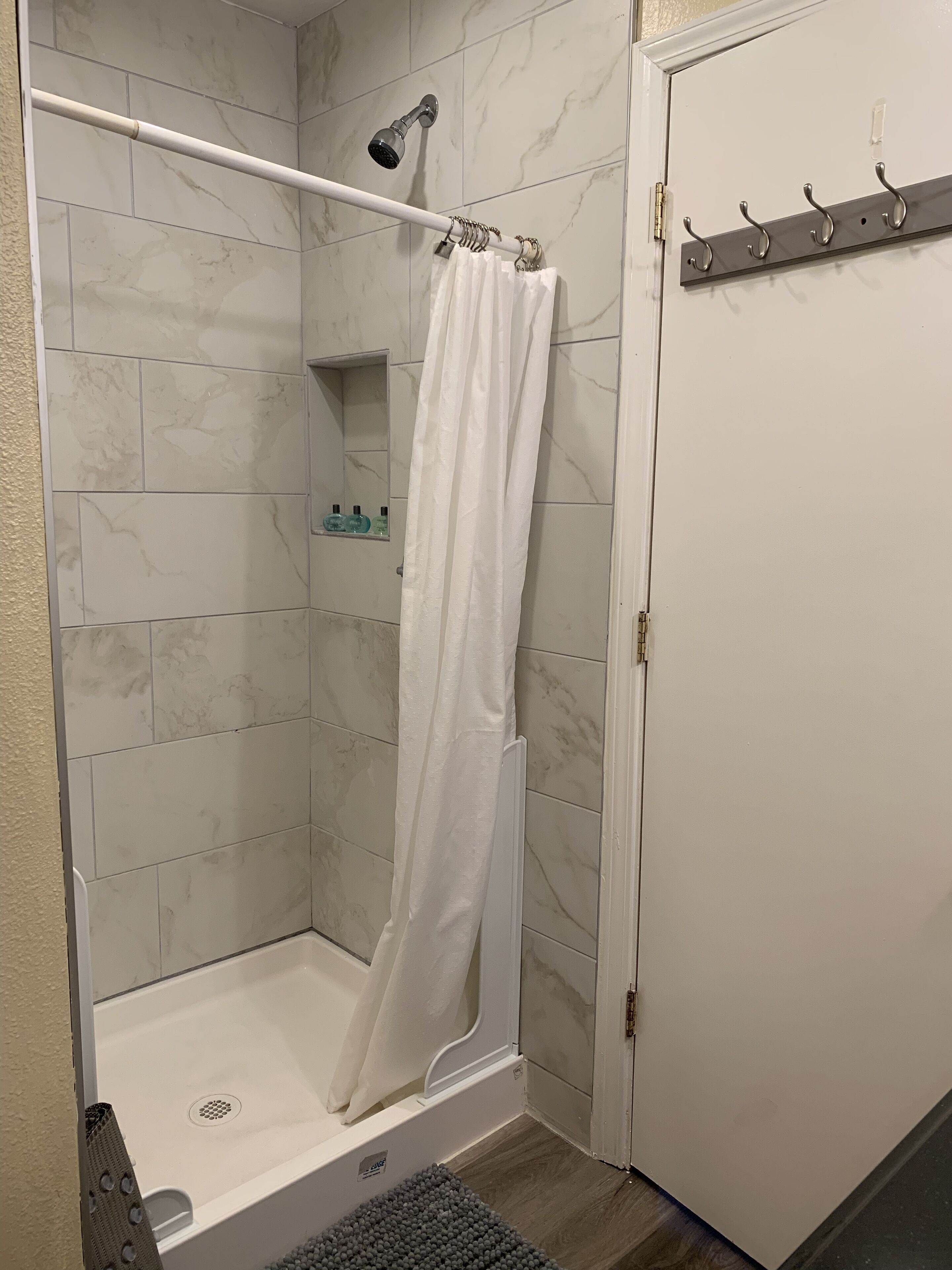 A walk-in shower with a white shower curtain, a handheld showerhead, and a tiled wall.