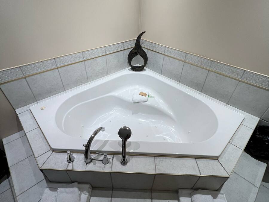 A corner bathtub with a black decorative object on the wall, a towel rack, and a trash bin.