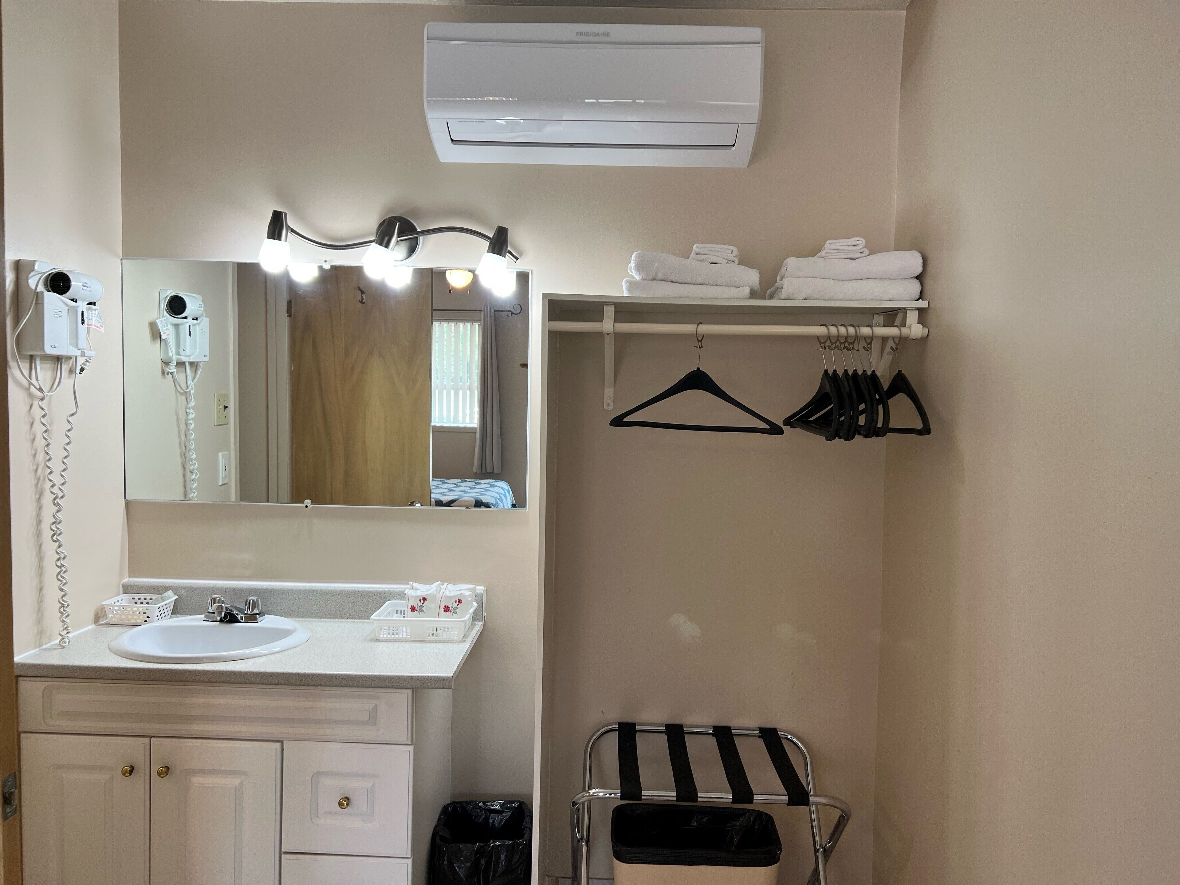A bathroom with a sink, mirror, lights, towel rack, and a trash bin.