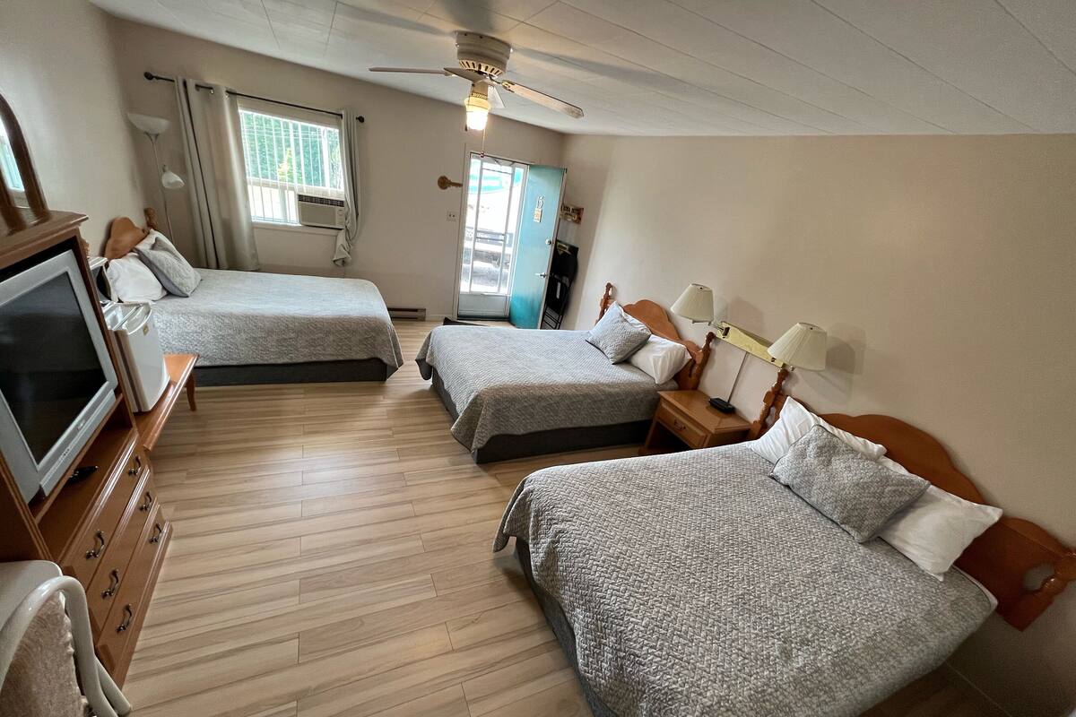 A hotel room with two beds, a TV, a desk, and a ceiling fan.