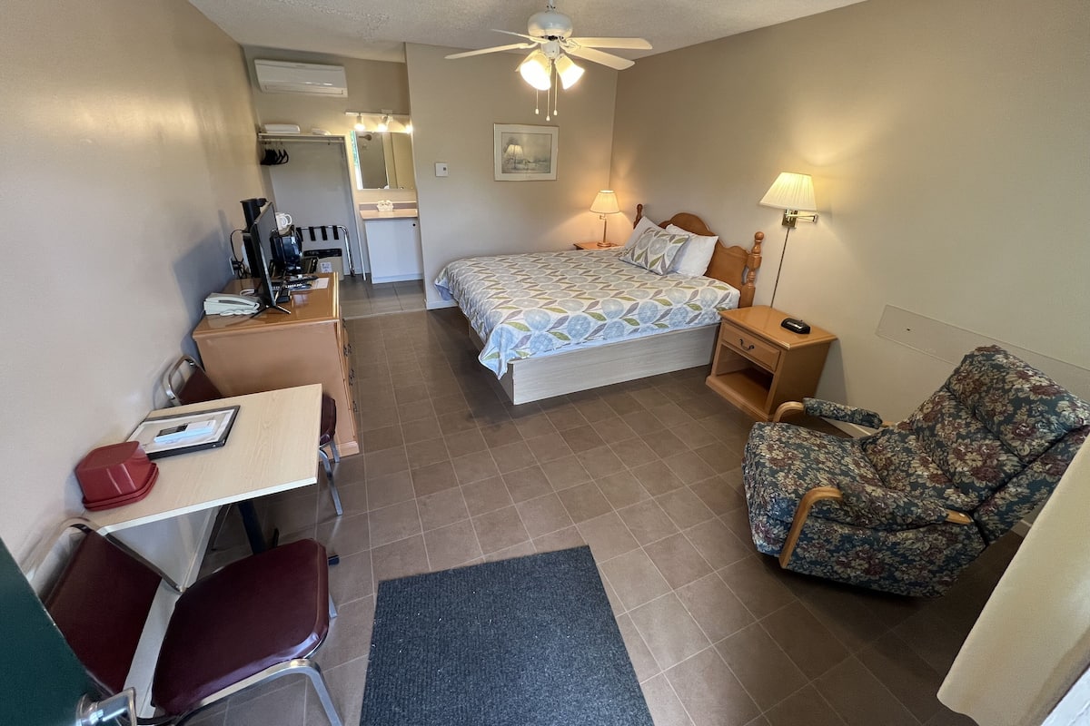 A hotel room with a bed, desk, chair, and a small kitchenette.