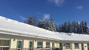 Un edificio de dos pisos con fachada de piedra y revestimiento, múltiples ventanas y techo cubierto de nieve.
