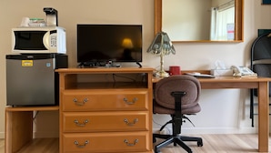 Habitación de hotel con escritorio de madera, televisor, refrigerador, silla, lámpara, teléfono y espejo.