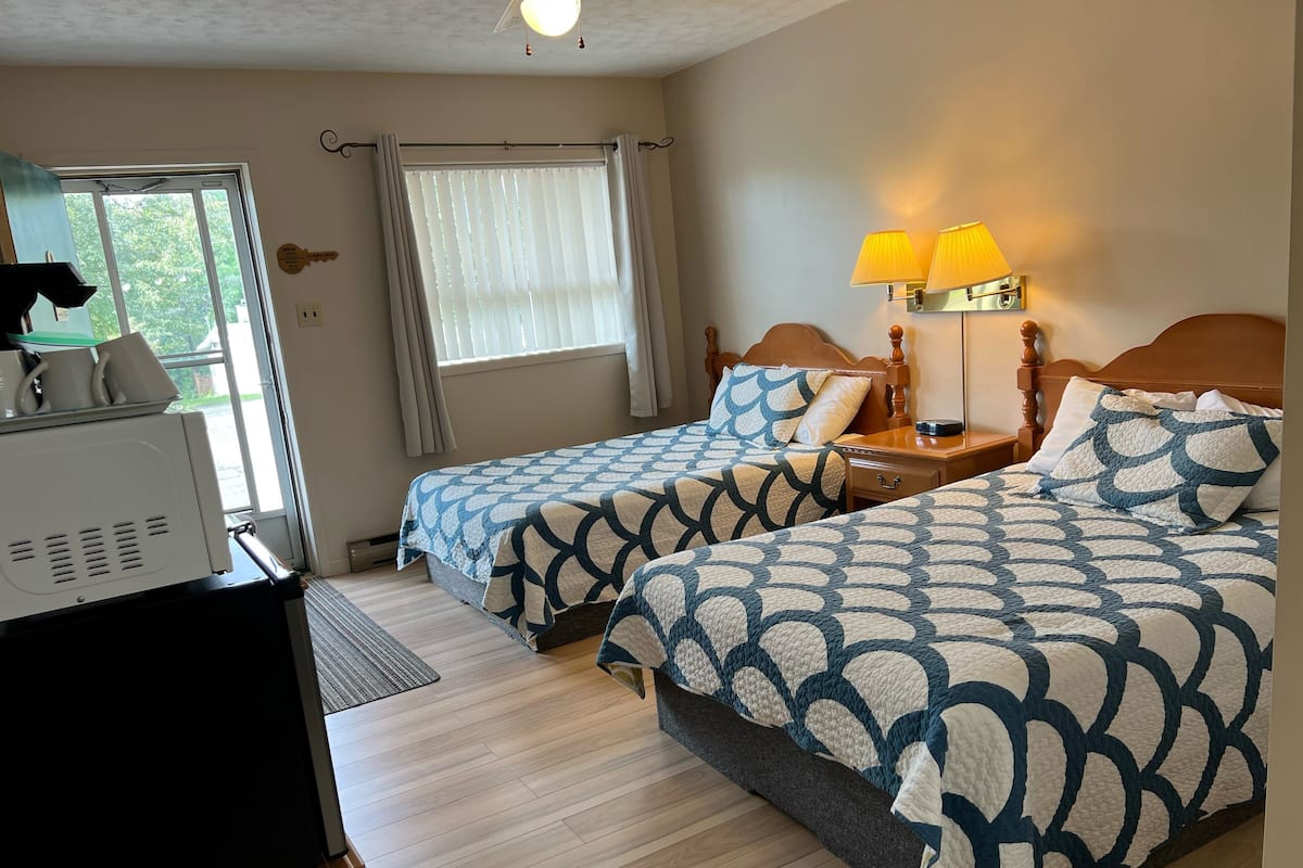 A hotel room with two beds, a desk, a lamp, and a window with curtains.