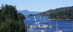 A marina with boats and yachts docked, surrounded by dense forest and mountains in the background. - Enchanter Oceanview Suites (Madeira Park)