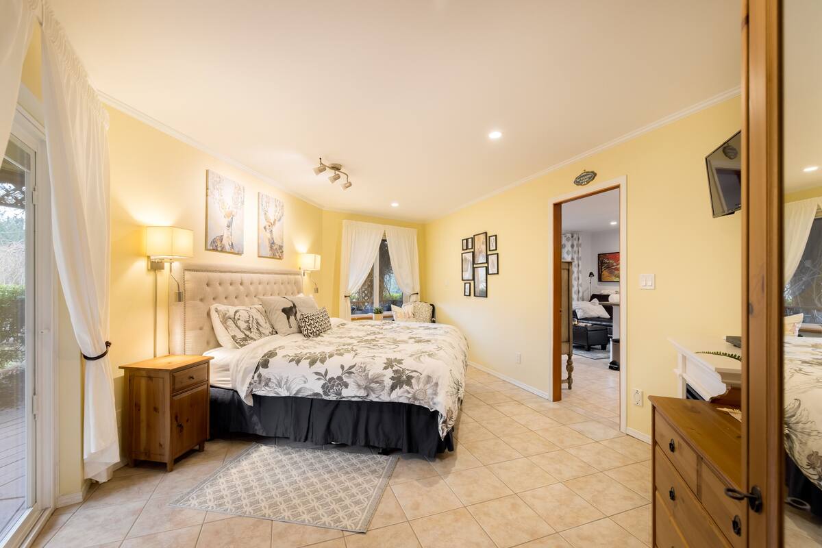 Un dormitorio con cama, mesitas de noche, un espejo y una puerta que da a otra habitación.