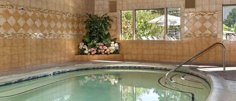 An indoor swimming pool with tiled walls, a metal ladder, and a potted plant with flowers.