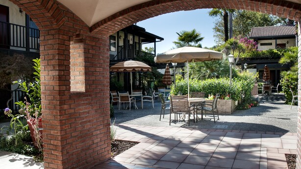 Un espacio de patio al aire libre con columnas de ladrillo, una mesa cubierta con sillas y vistas a un edificio al fondo.