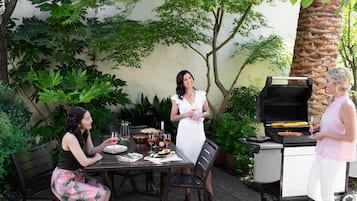 Un patio al aire libre con una mesa lista para comer, una parrilla y abundante follaje de fondo.