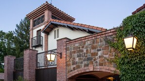 Una casa de dos plantas con fachada de piedra, puerta de garaje negra y un balcón con barandilla de hierro forjado.