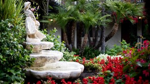 Un jardín con una estatua, una fuente escalonada y diversas plantas.