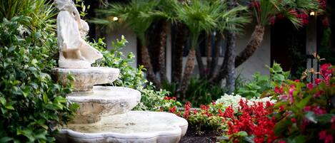 A garden with a statue, a tiered fountain, and various plants.