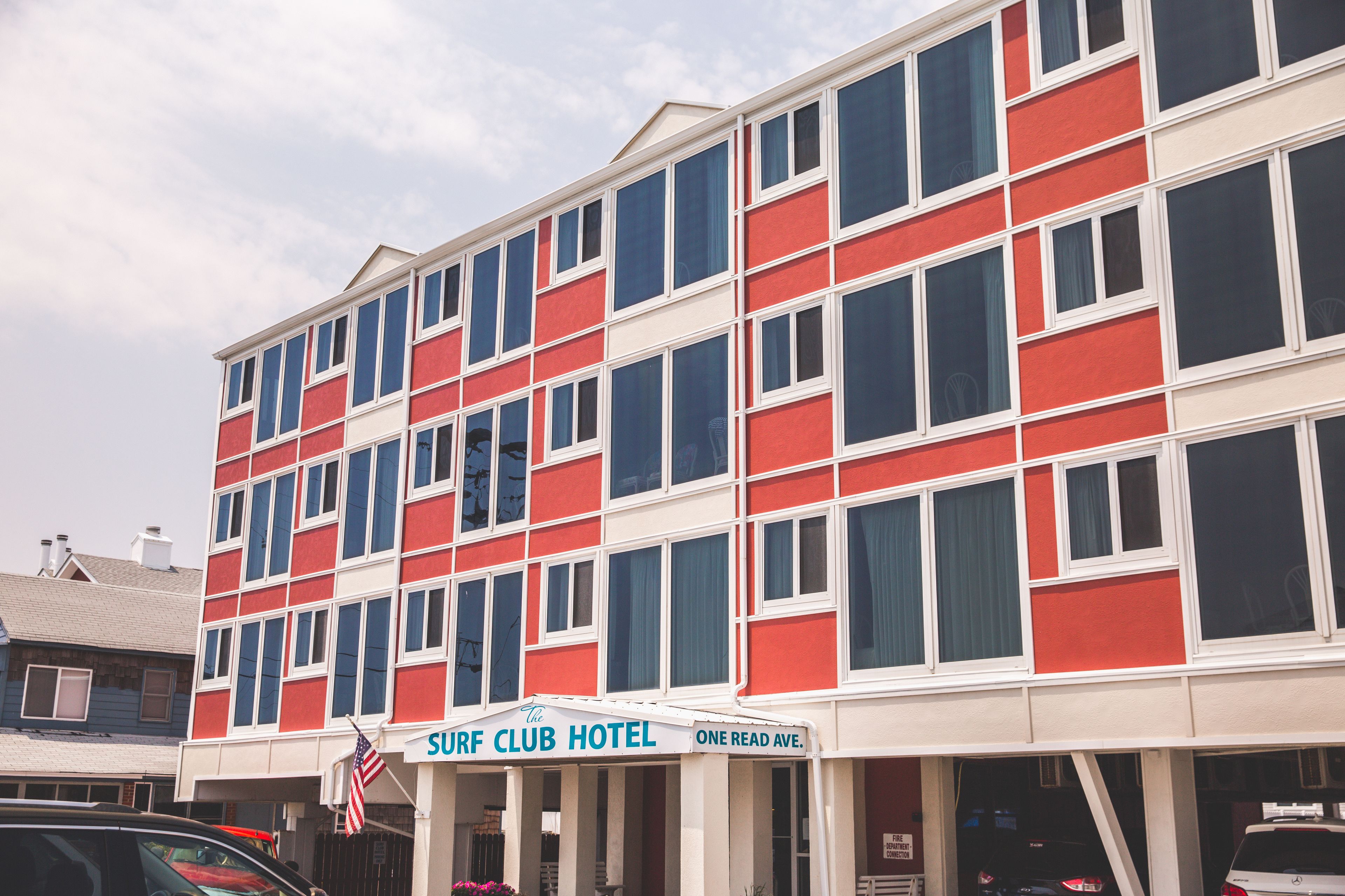 Un edificio de varios pisos con fachada roja y blanca, con el letrero "Surf Club Hotel" en la planta baja.