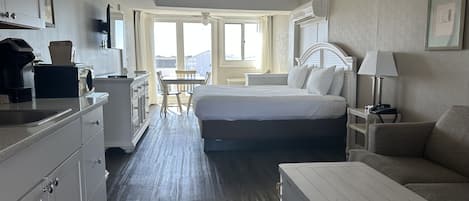 A hotel room with a bed, a desk, a chair, a sofa, a coffee maker, and a television.