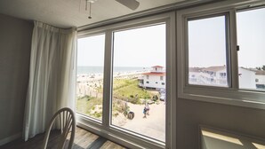 A room with a large window overlooking a beach and a building. - Surf Club Oceanfront Hotel (Dewey Beach)
