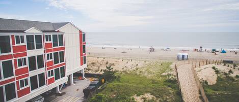 A beachfront hotel with a red and white facade, a sandy beach in the background, and a clear view of the ocean.
