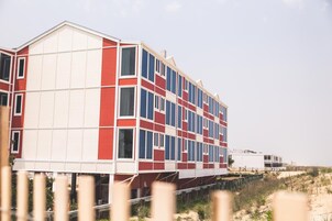 Ein mehrgeschossiges Gebäude mit einer markanten rot-weißen Fassade, in der Nähe eines Strandes mit Sanddünen gelegen.