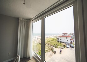 A room with a large window overlooking a beach and a building.