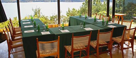 Mesa preparada para seis personas con vista a un lago y colinas al fondo.