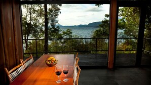 A wooden dining table with two wine glasses and a fruit bowl, overlooking a lake with trees and hills. - Hotel Antumalal (Pucón)
