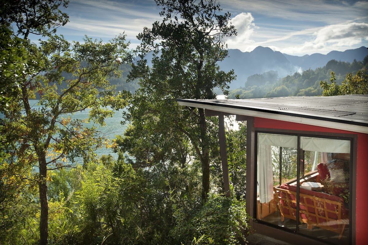 Un bâtiment moderne doté de grandes fenêtres, entouré d’une végétation luxuriante et avec des montagnes en toile de fond.
