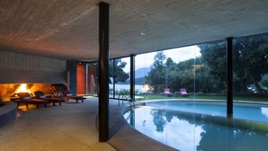 A modern indoor pool area with a fire feature, lounge chairs, and a view of the outdoors. - Hotel Antumalal (Pucón)