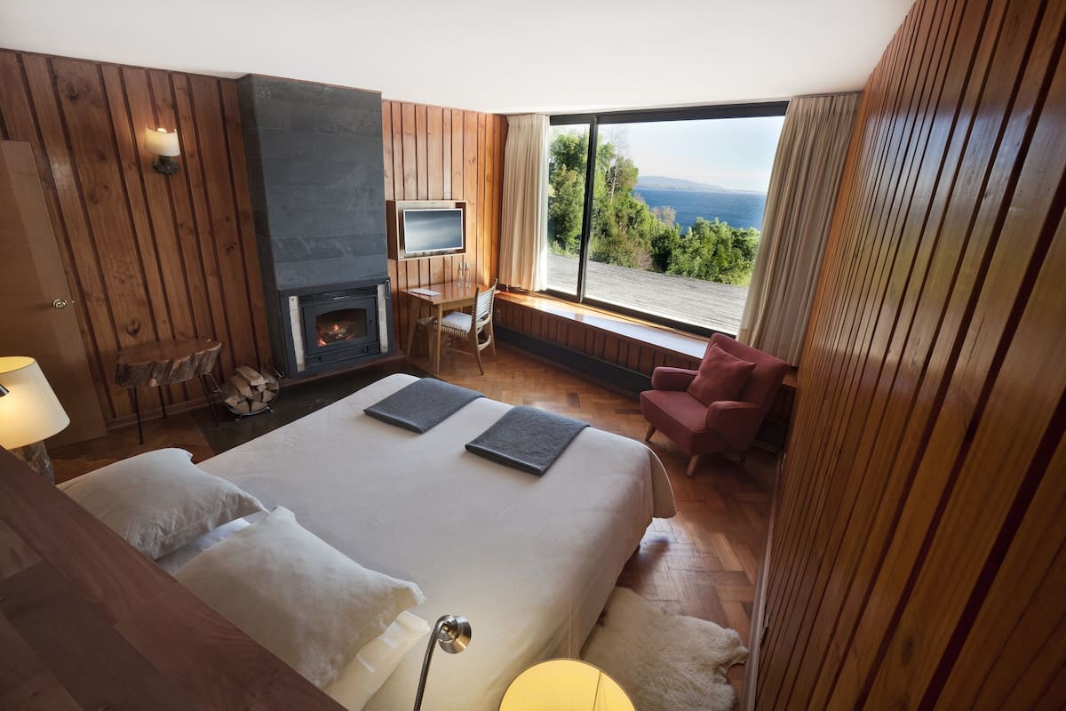 Une chambre avec un grand lit, une télévision, une cheminée et une vue sur l’extérieur.
