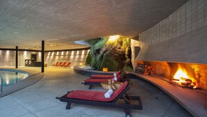 A spa area with a pool, lounge chairs, a fire feature, and a moss-covered wall. - Hotel Antumalal (Pucón)