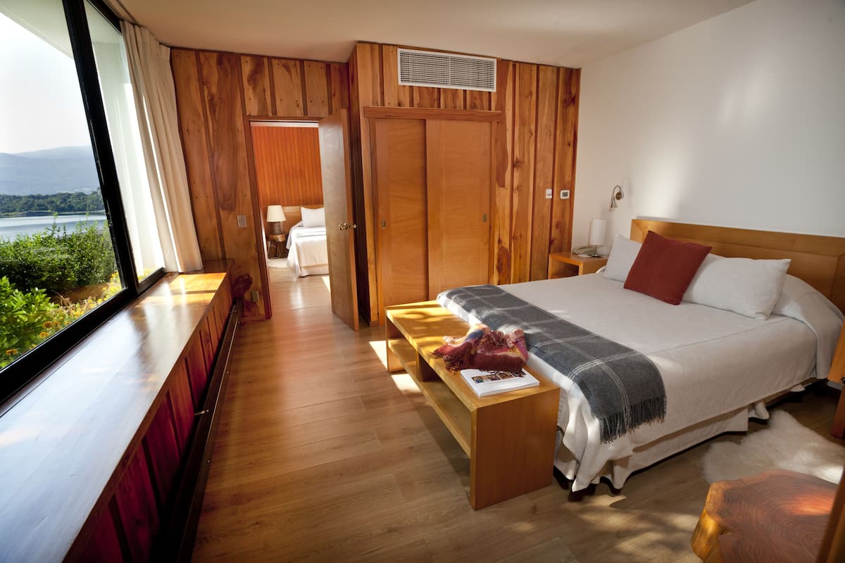 Une chambre avec un grand lit, un plancher en bois, un banc et une vue sur un lac.