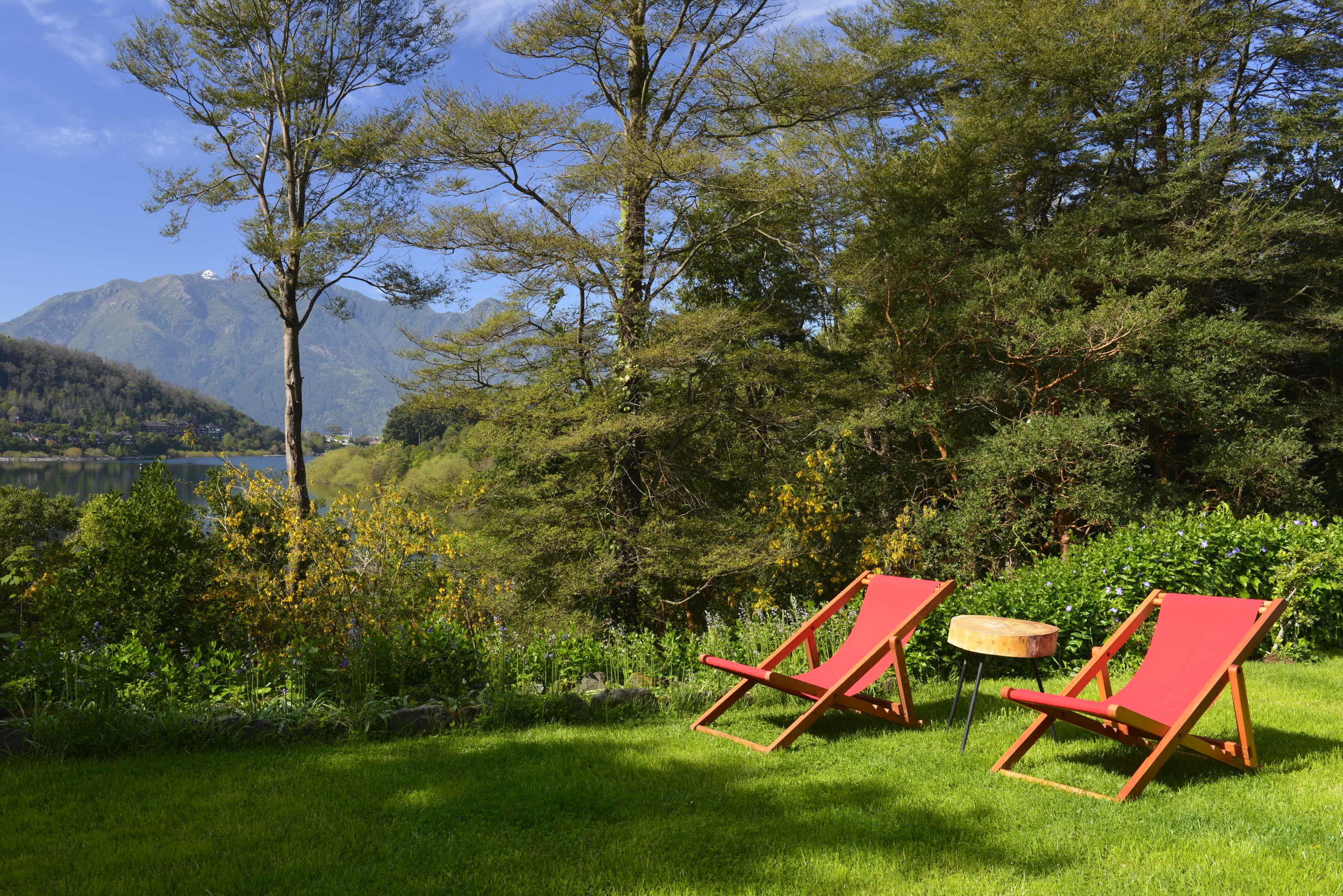 Two red lounge chairs in a grassy area with a mountain and lake in the background.
