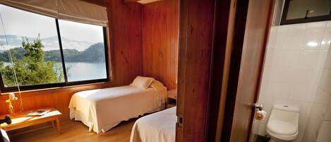 Une chambre avec deux lits, un plancher en bois, une fenêtre donnant sur un lac et une salle de bain avec des toilettes.