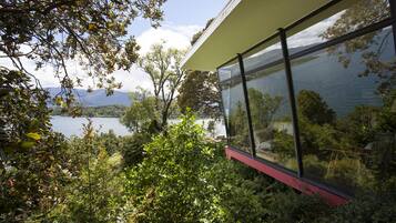 Ein modernes Gebäude mit großen Glasfenstern mit Blick auf einen See und Berge.