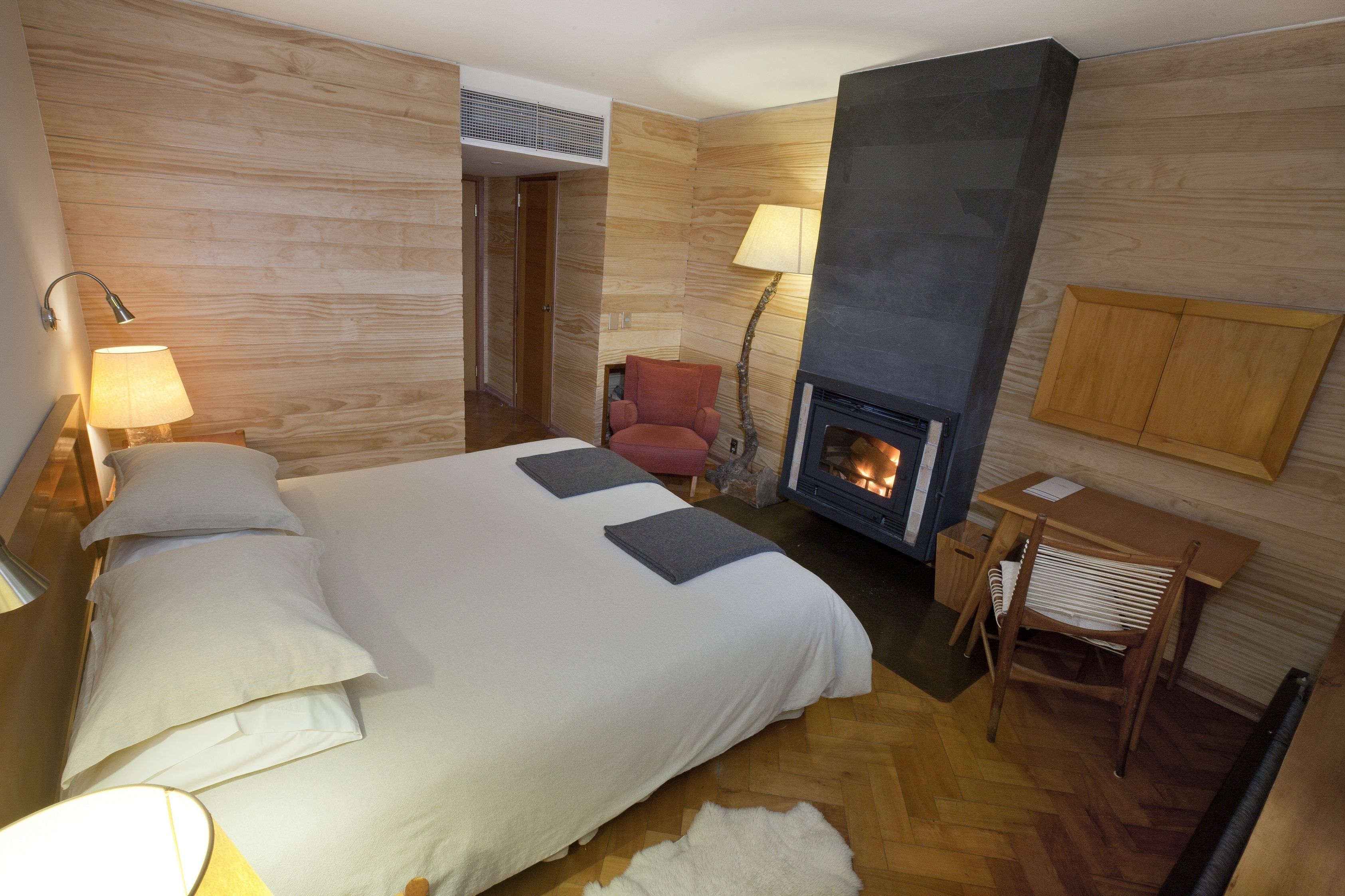 Un dormitorio con una cama, dos lámparas de noche, una chimenea, una mesita y una silla.