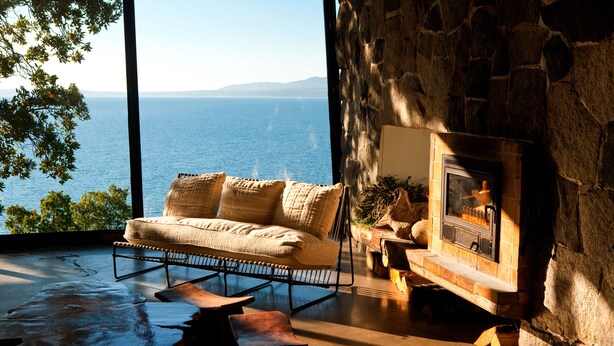 A cozy living room with a stone fireplace, a comfortable sofa, and a view of the sea. - Hotel Antumalal (Pucón)