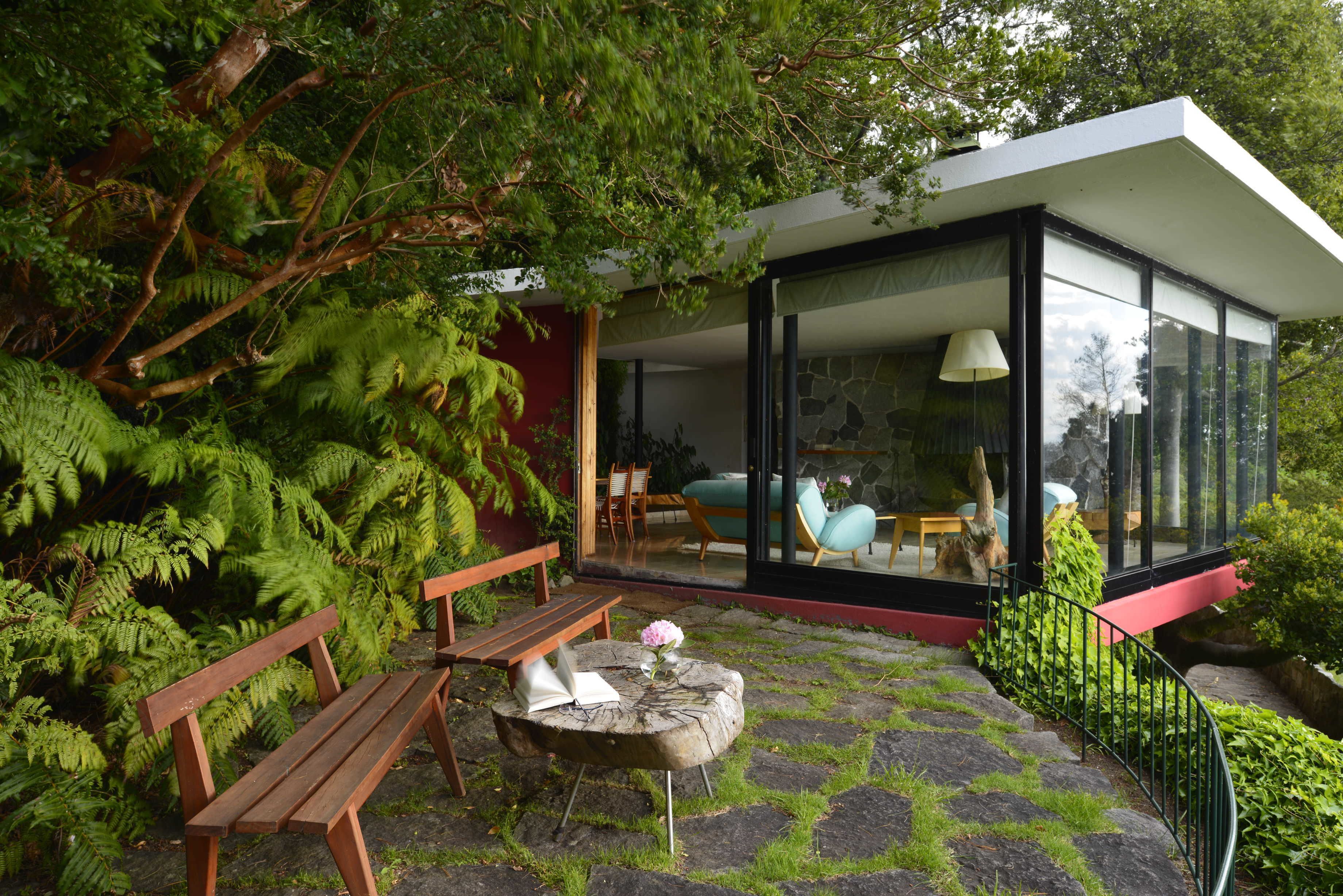 Une maison moderne dotée d’une véranda en verre, de meubles en bois et d’une végétation luxuriante.