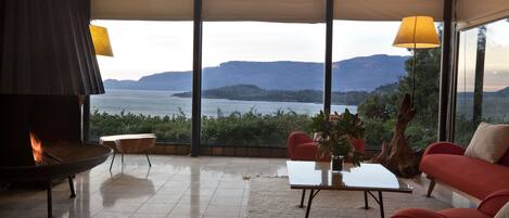 A modern living room with a fireplace, red sofa, and a view of a lake and mountains.