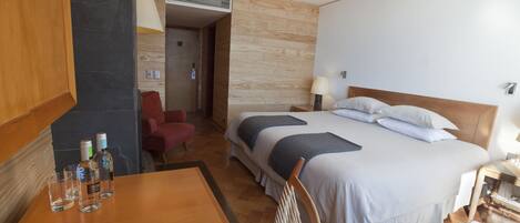 A hotel room with a bed, a wooden table with glasses and a menu, a chair, and a desk lamp.