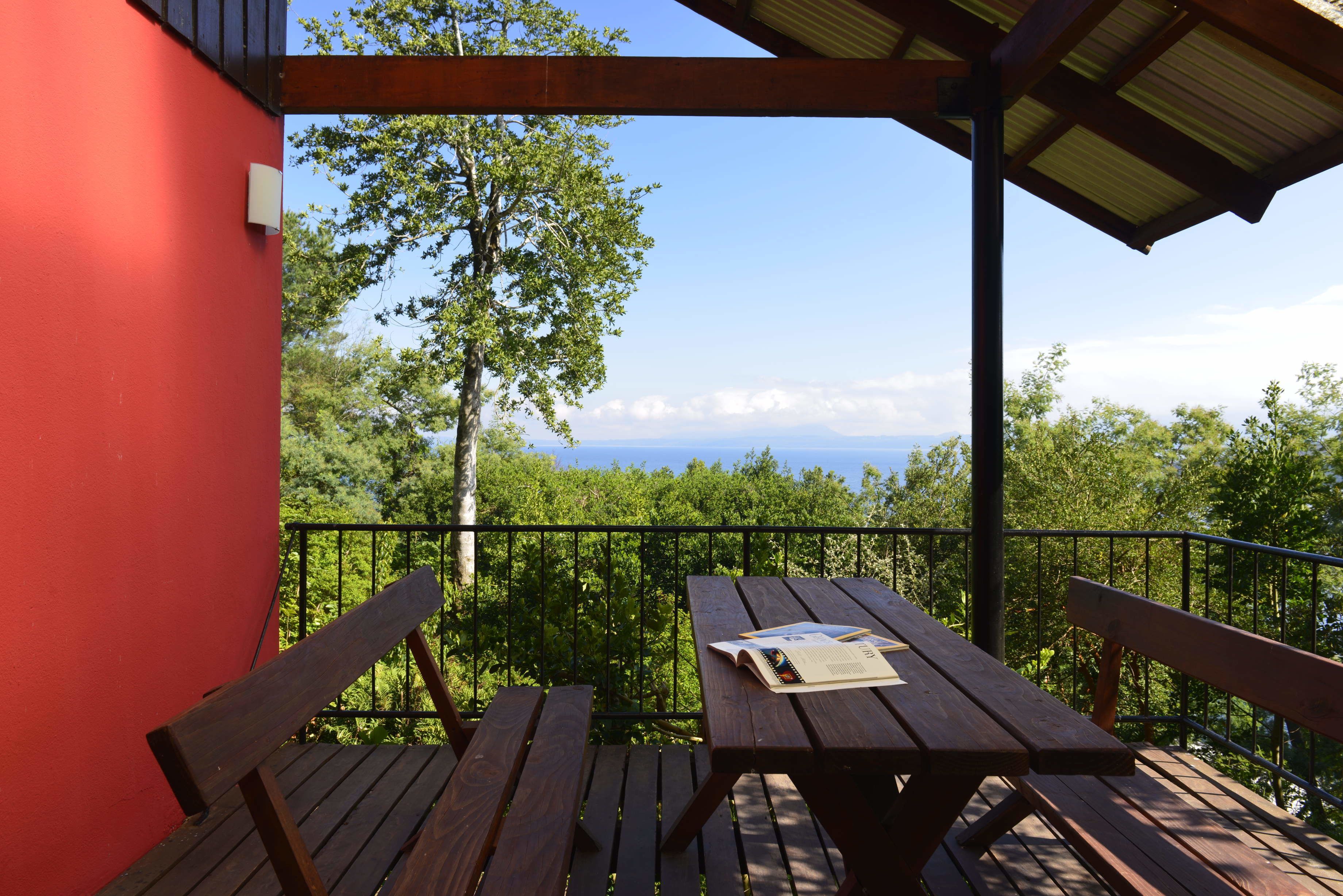 A wooden deck with a picnic table and benches, overlooking a forested area and distant mountains.