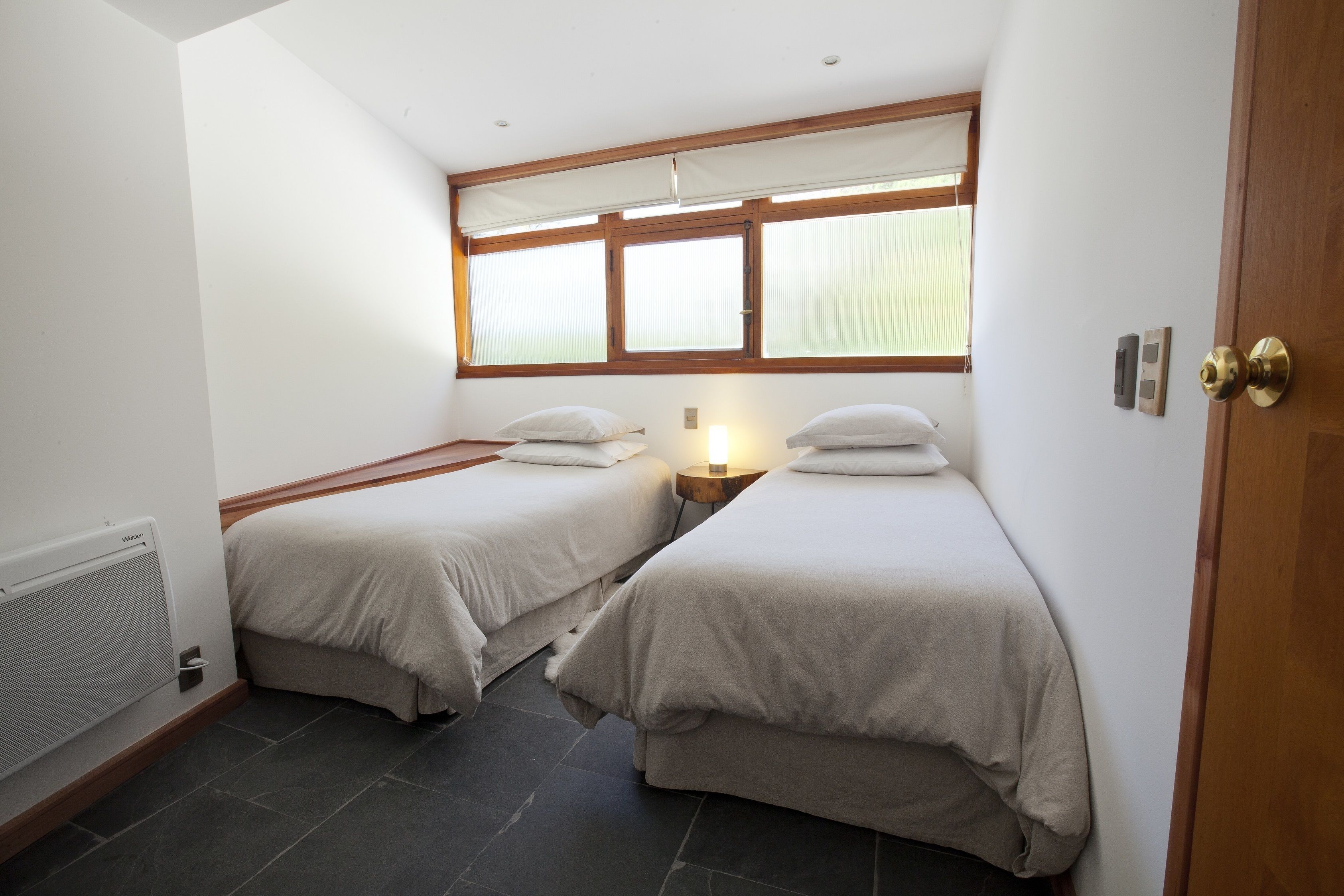 Una habitación con dos camas, una ventana con persianas, un radiador y una puerta de madera.