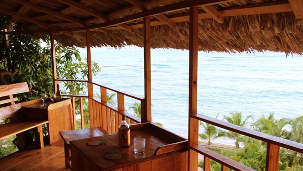 Una terraza de madera con techo de paja que da a la playa.