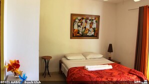 Una habitación de hotel con cama, ventilador de techo, un cuadro, una mesita y una lámpara.