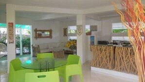 Un espacio habitable amplio y luminoso, con mesa de comedor de vidrio, sillas verdes, sofá y zona de cocina con barra.