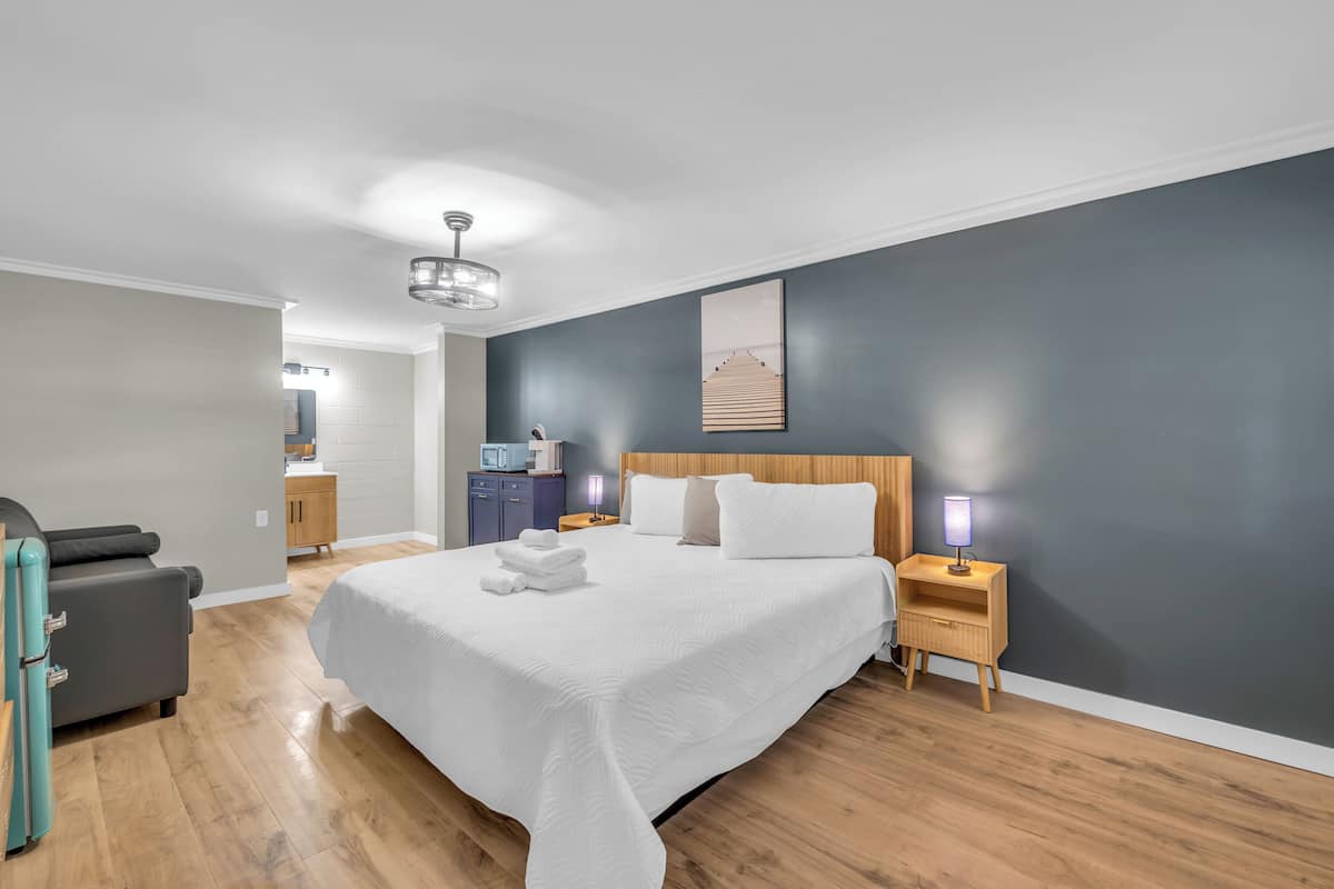 A modern bedroom with a large bed, wooden headboard, bedside tables with lamps, a gray wall, and a wooden floor.