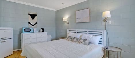 A bedroom with a bed, a dresser, a microwave, and a nightstand.