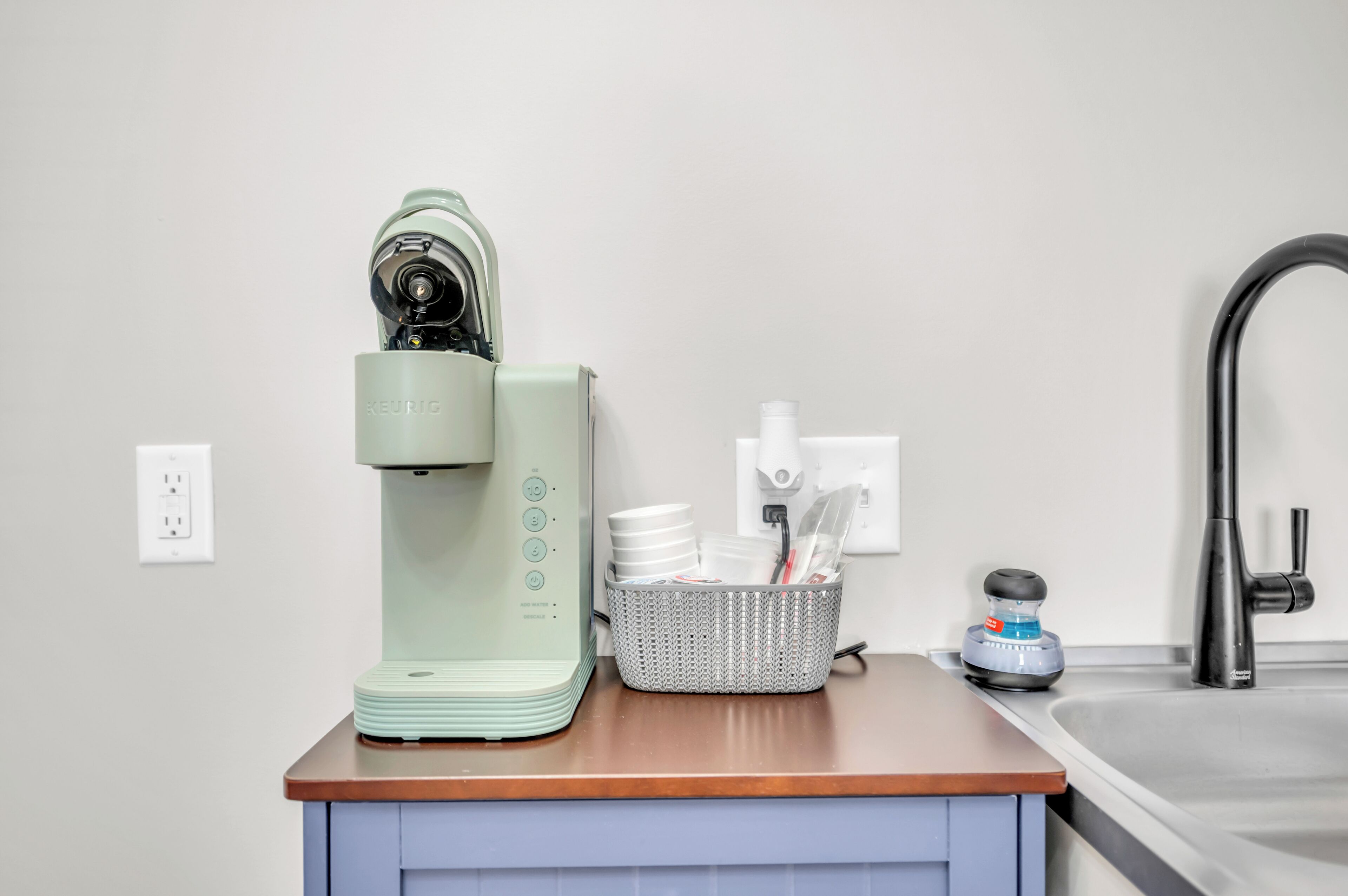 A kitchen with a coffee maker, a basket of dishes, and a sink.