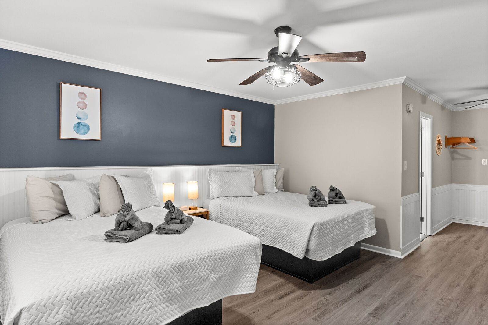 Une chambre d’hôtel avec deux lits, un ventilateur de plafond et des œuvres d’art accrochées aux murs.