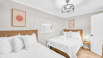 Habitación de hotel con dos camas, ropa blanca, cabecero de mimbre, una lámpara de araña moderna y una mesita de noche con lámpara.